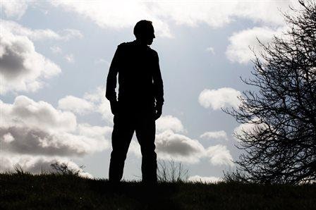 Silhouette of a man looking to the side with sky and clouds behind. 